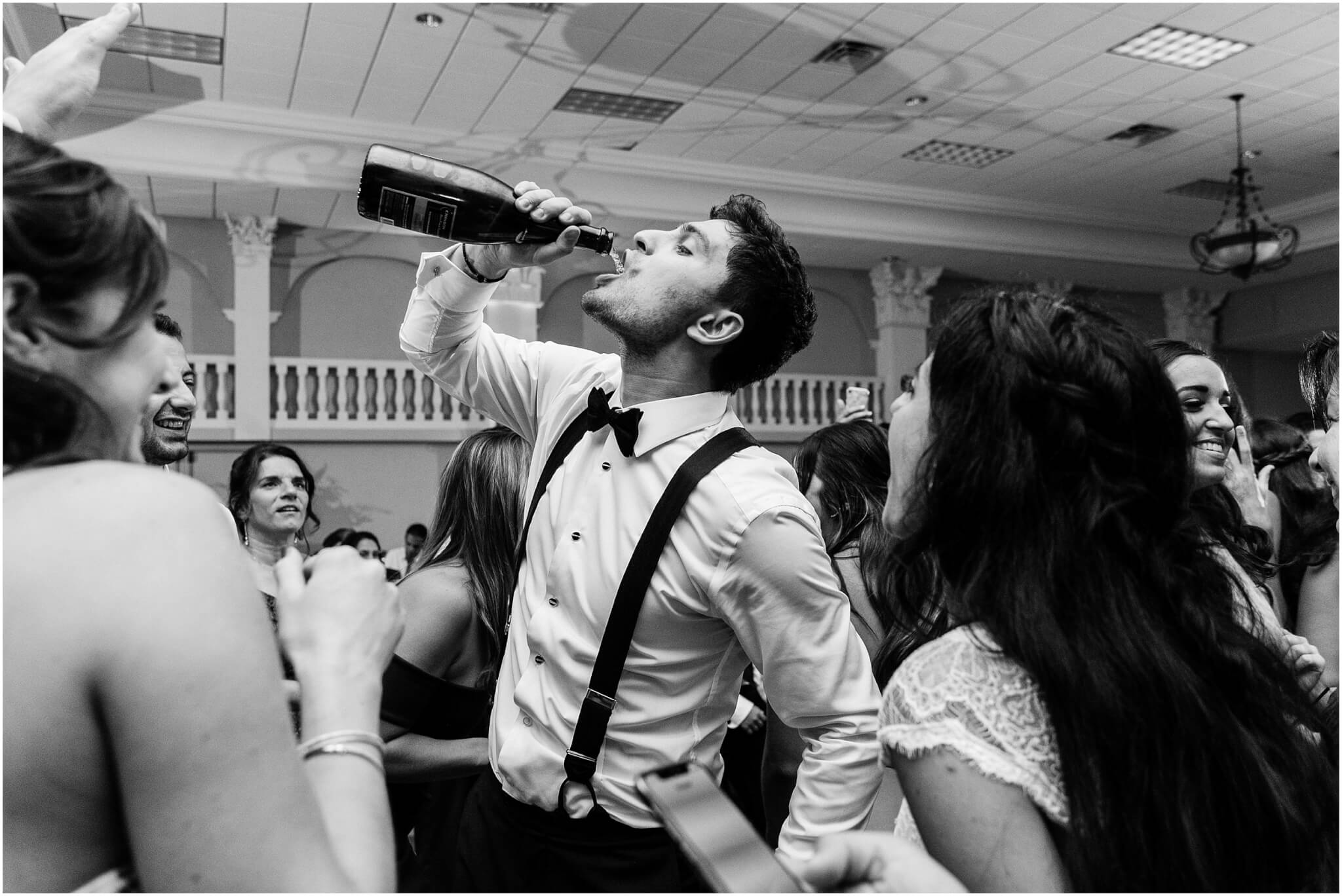 Groom drinking from a champagne bottle I wedding reception