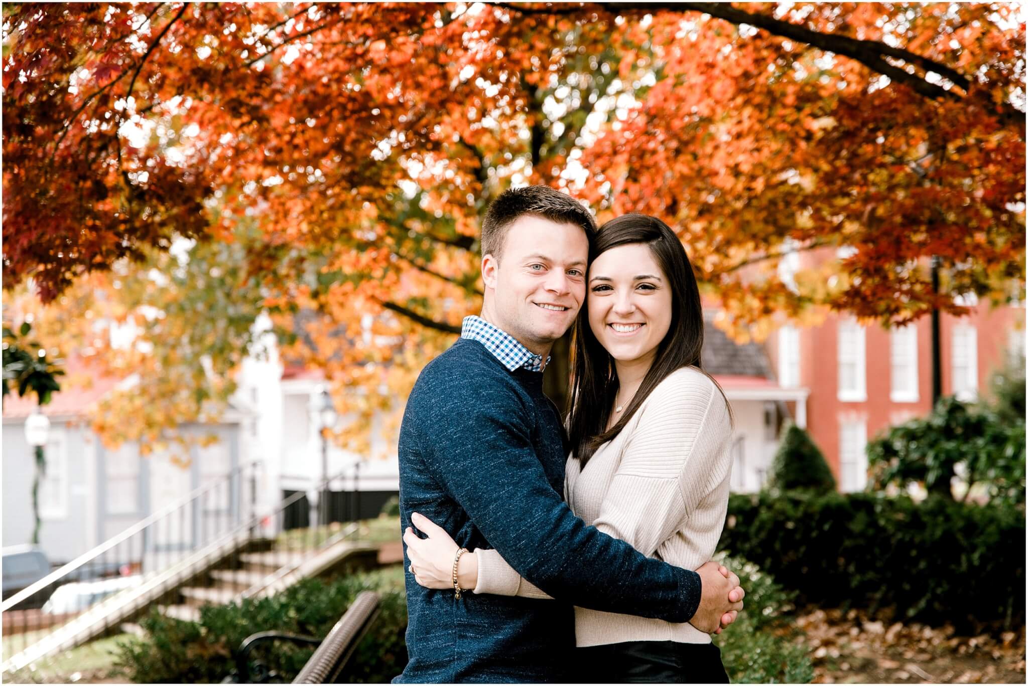 couple smiling looking at the camera in front of gorgeous fall maple