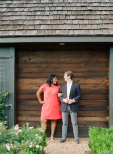 Couple arm in arm against wood backdrop looking at each other and smiling