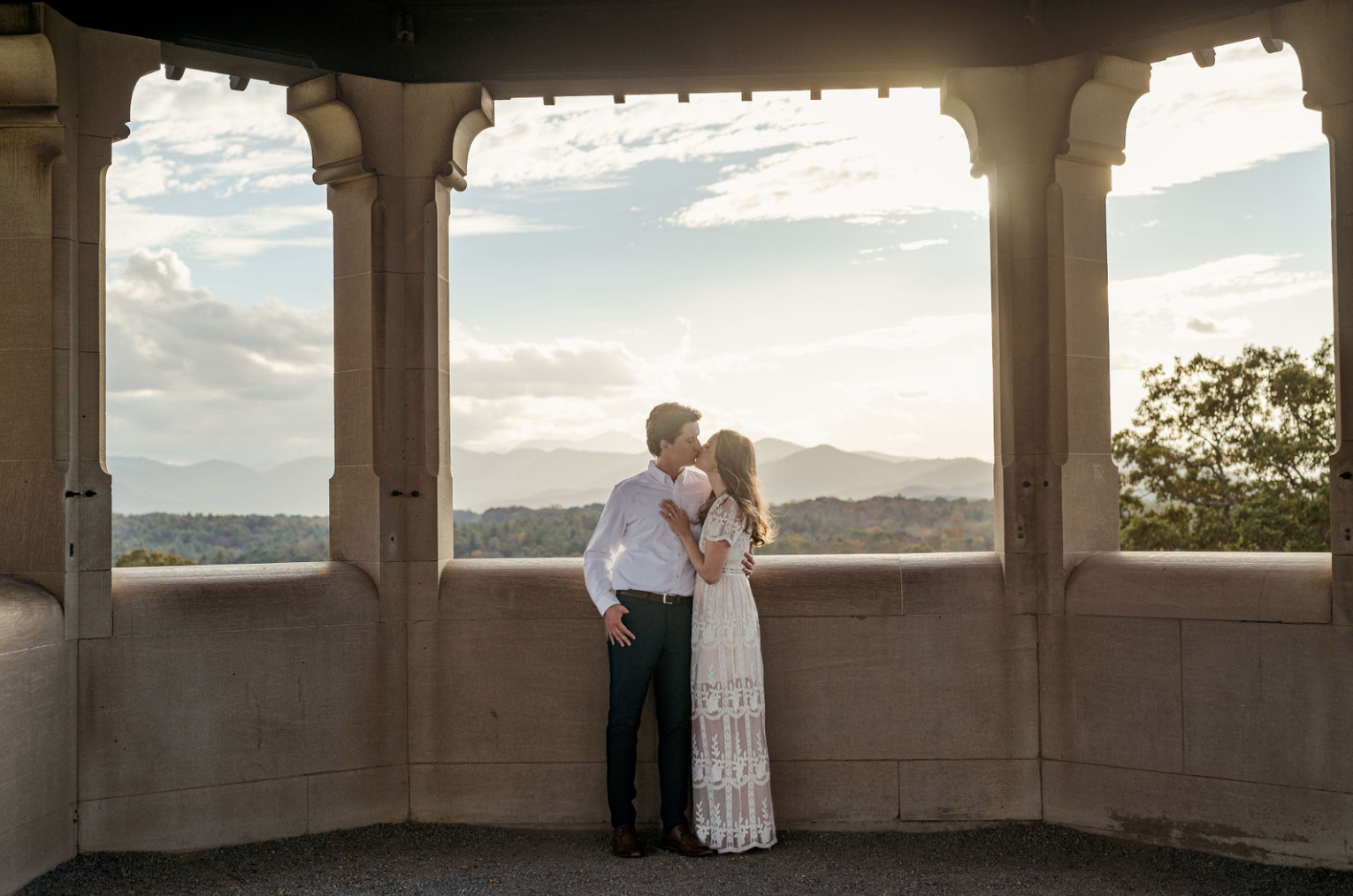 Couple kissing on rooftop at Biltmore Estate with mountains in background