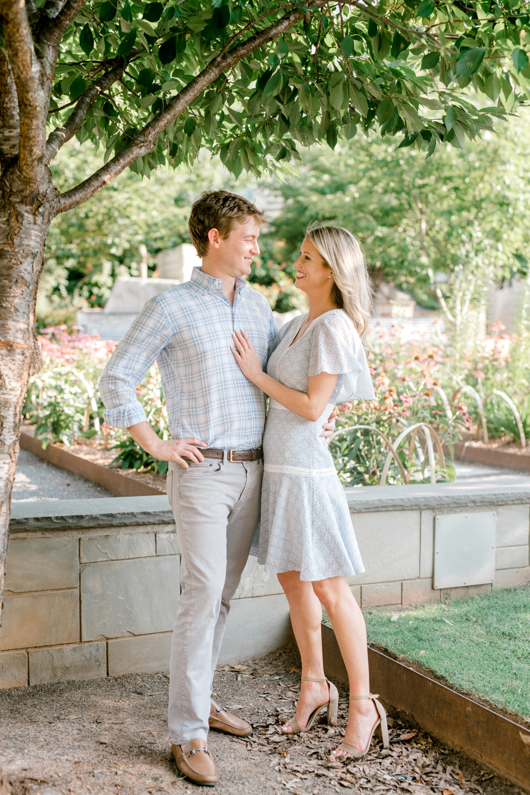 Couple smiling outside under tree wearing dusty blue and neutral outfits